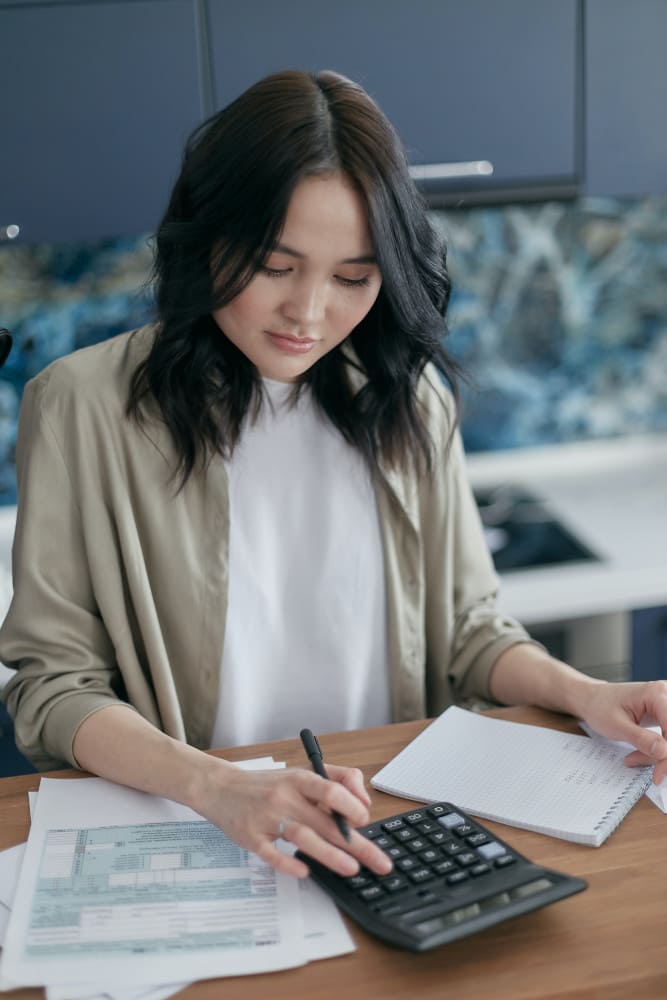 Une femme fait ses comptes à la calculatrice, devant des formulaires et un carnet de notes